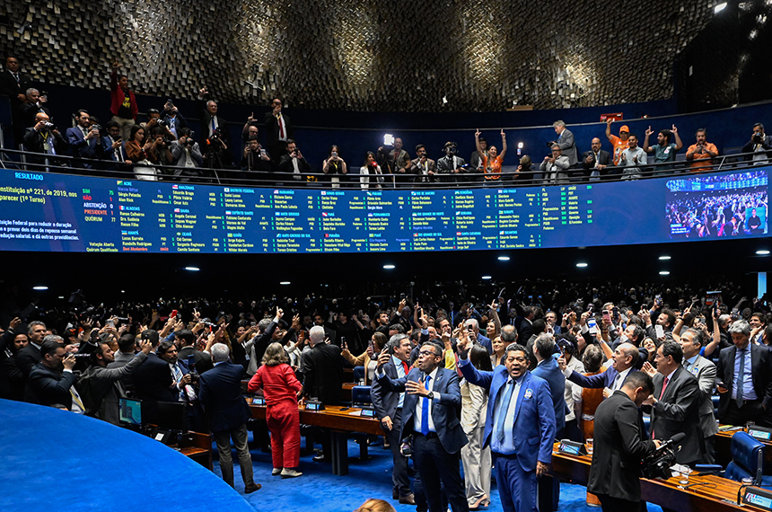 Parlamentares e convidados de pé comemoram no Plenário do Senado, com o painel de votação ao fundo.