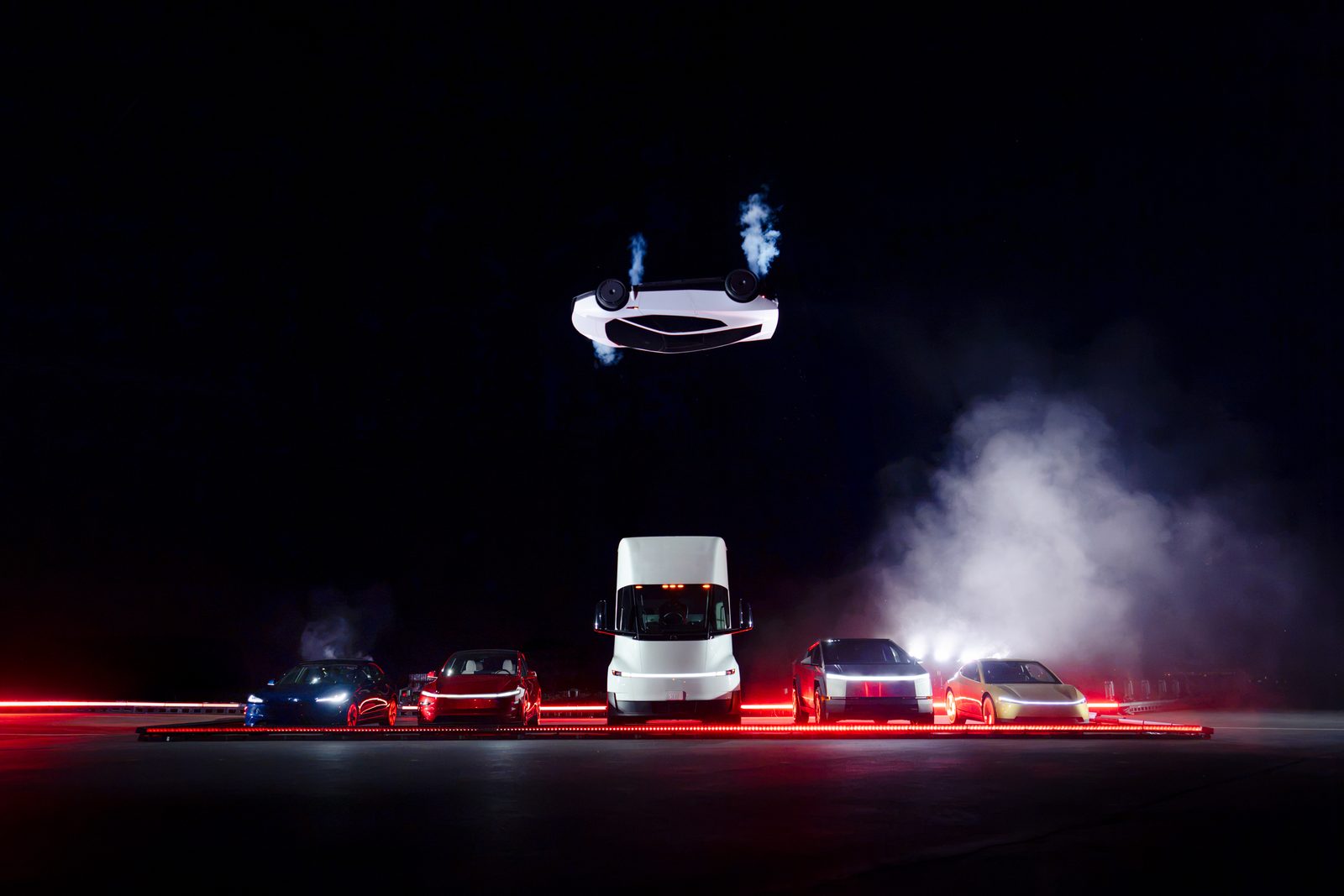 Carro branco de cabeça para baixo no ar sobre uma fila de carros Tesla e um caminhão Semi, com fumaça, em ambiente escuro